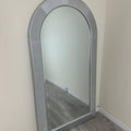 Silver-framed mirror leaning against a white wall.