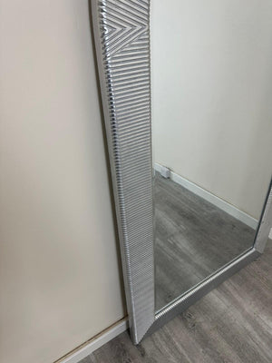 Full-length mirror with decorative frame on a plain wall.