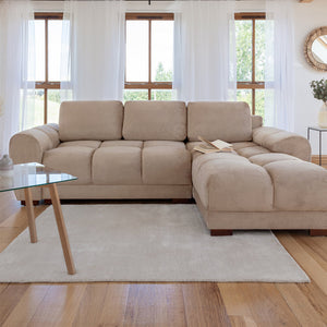 Beige sectional sofa in a living room with large windows and a glass coffee table.