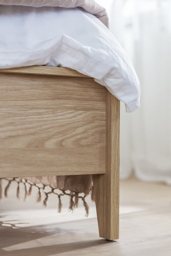Wooden bed frame with white bedding on a light wooden floor.