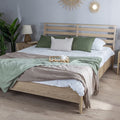 Wooden bed with green and brown bedding in a room with plants and lamps.