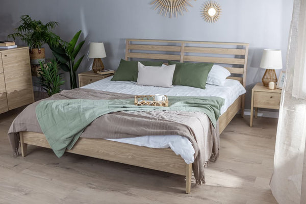Wooden bed with green and brown bedding in a room with plants and lamps.