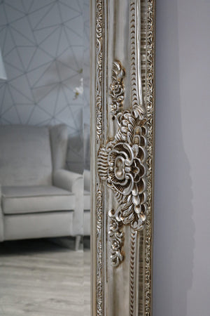 Decorative muted brownish-grey mirror with intricate designs in a room with a sofa and geometric wall.