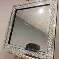 Decorative mirror with a sparkling frame on an easel against a plain wall.
