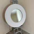 Decorative round mirror with intricate design on a stand against a beige wall.