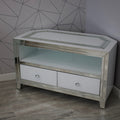 Corner TV stand with glass top and white drawers against a geometric-patterned wall.