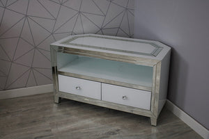Corner TV stand with glass top and white drawers against a geometric-patterned wall.