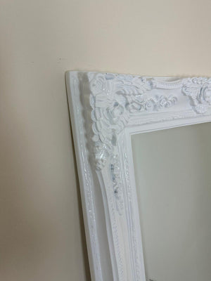 Decorative white mirror with intricate frame against a plain wall