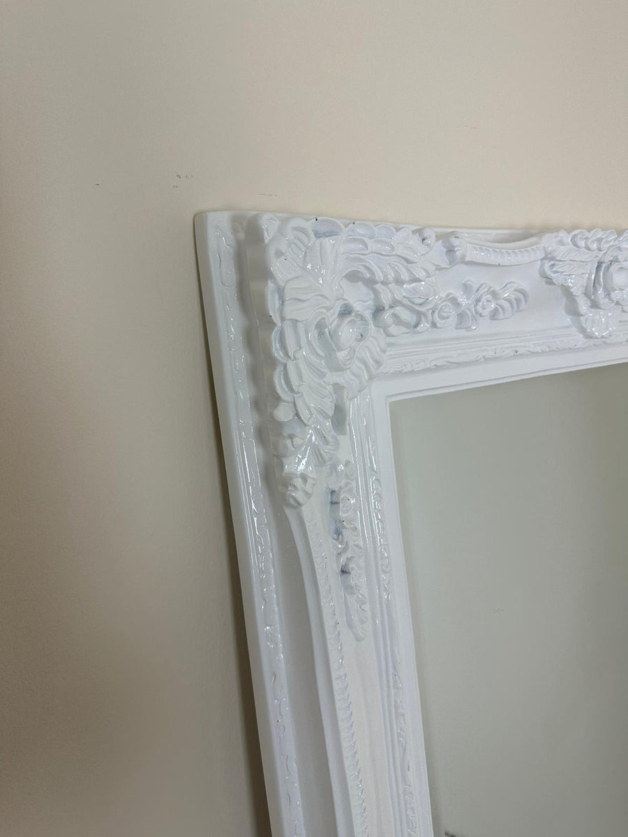 Decorative white mirror with intricate frame against a plain wall