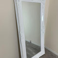 White ornate mirror leaning against a beige wall.