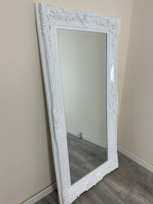White ornate mirror leaning against a beige wall.
