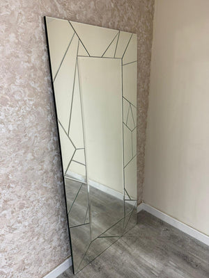 Tall mirror with geometric frame leaning against a textured wall.
