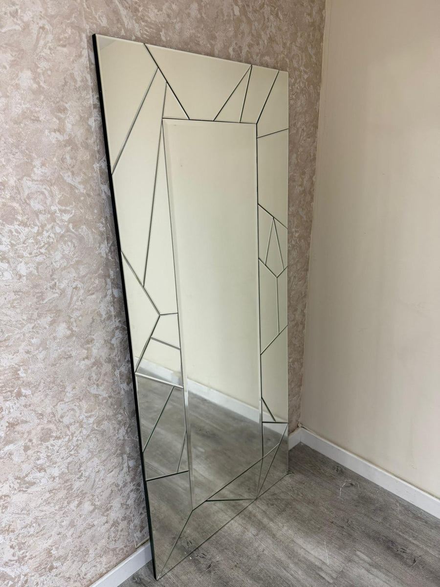 Tall mirror with geometric frame leaning against a textured wall.