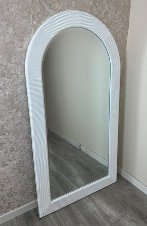 White woven mirror leaning against a textured wall.
