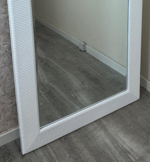 Floor mirror with a textured white frame on a gray floor.