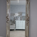 Decorative muted brownish-greyr mirror with intricate designs on a gray wall.
