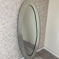 Oval mirror with decorative frame leaning against a textured wall.
