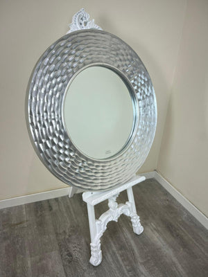 Decorative round mirror on a stand against a plain wall.