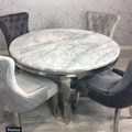 Round marble table with four gray upholstered chairs against a geometric patterned wall.