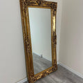 Decorative gold-framed mirror leaning against a white wall.