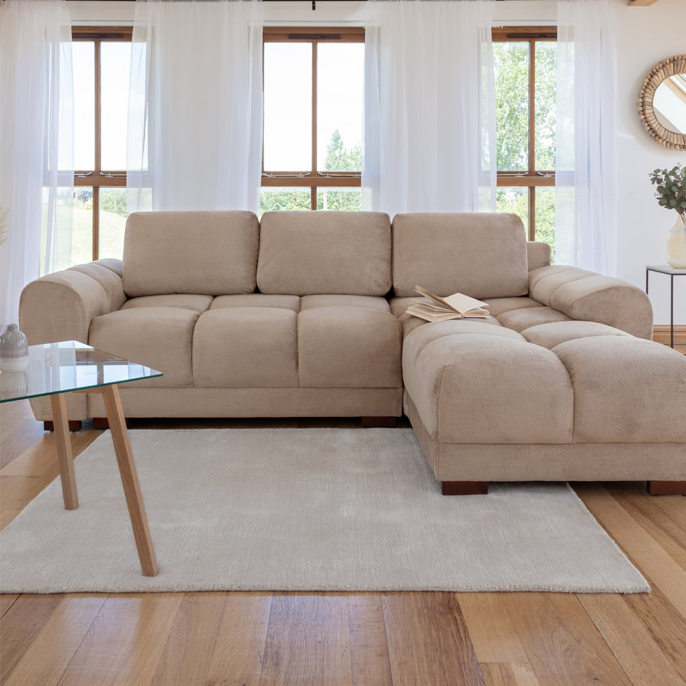 Beige sectional sofa in a living room with large windows and a glass coffee table.