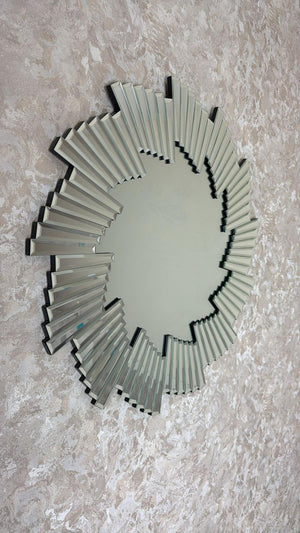 Decorative wall mirror with a sunburst design on a textured wall.
