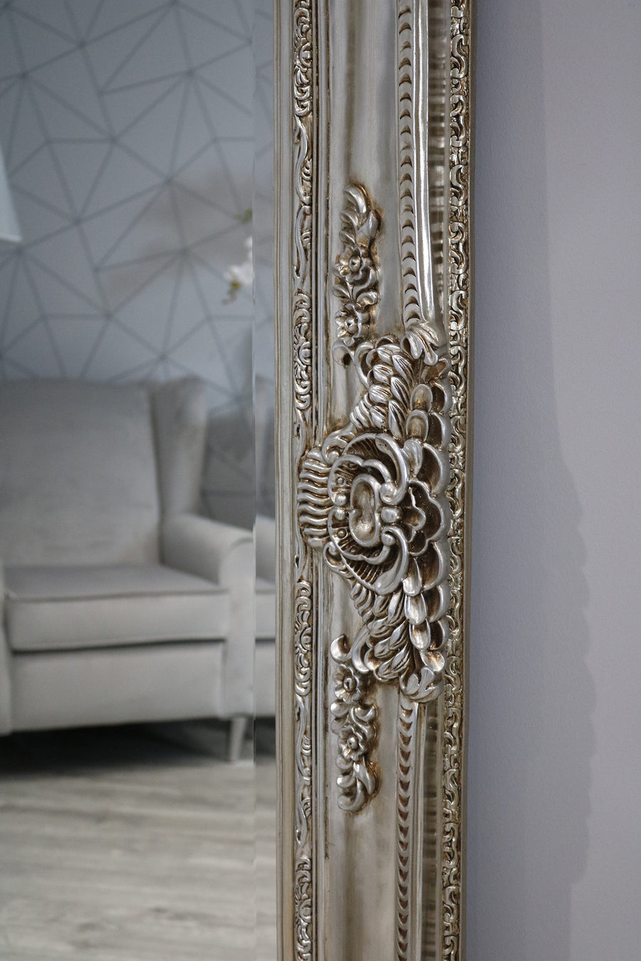 Decorative muted brownish-grey mirror with intricate designs in a room with a sofa and geometric wall.