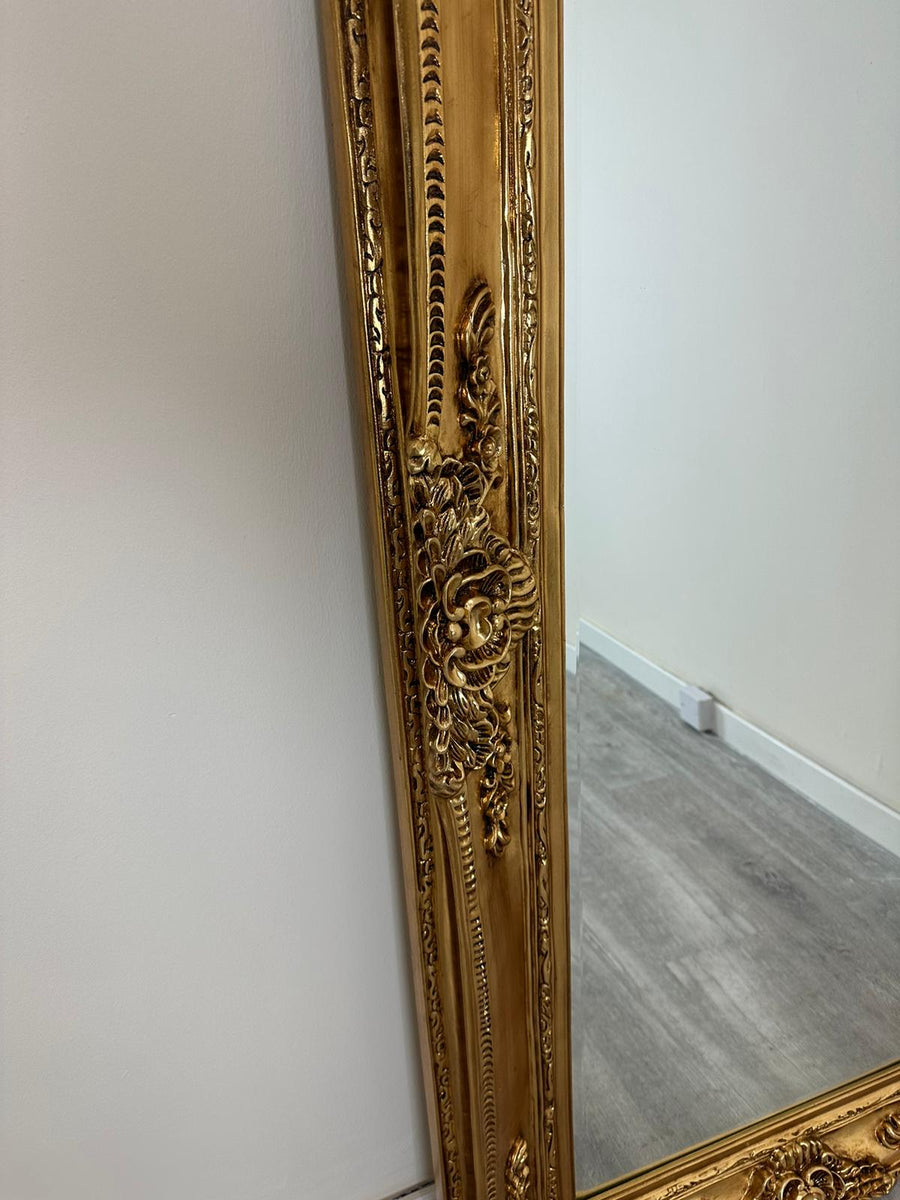 Decorative gold-framed mirror leaning against a white wall.