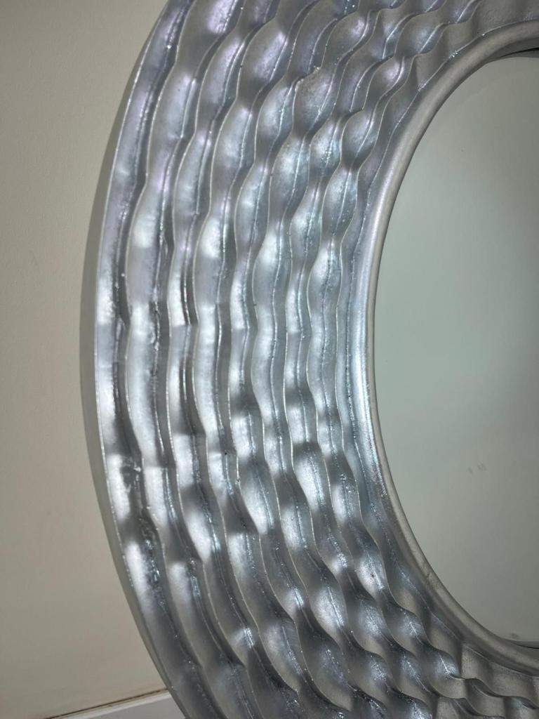 Round mirror with decorative silver frame on a plain background