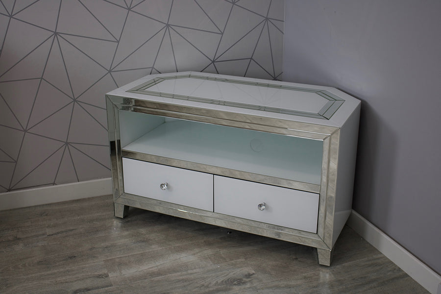 Corner TV stand with glass top and white drawers against a geometric-patterned wall.