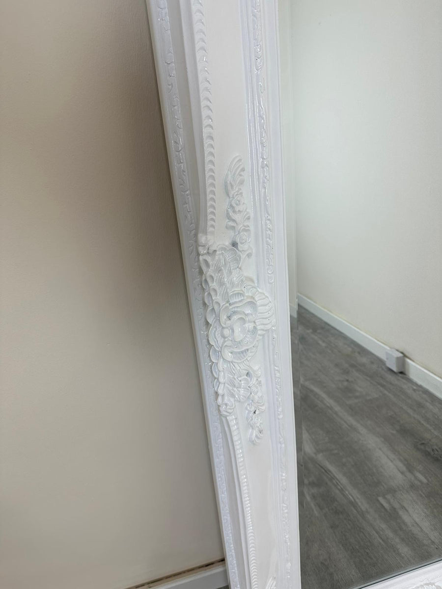 Decorative white frame leaning against a wall with a mirror.