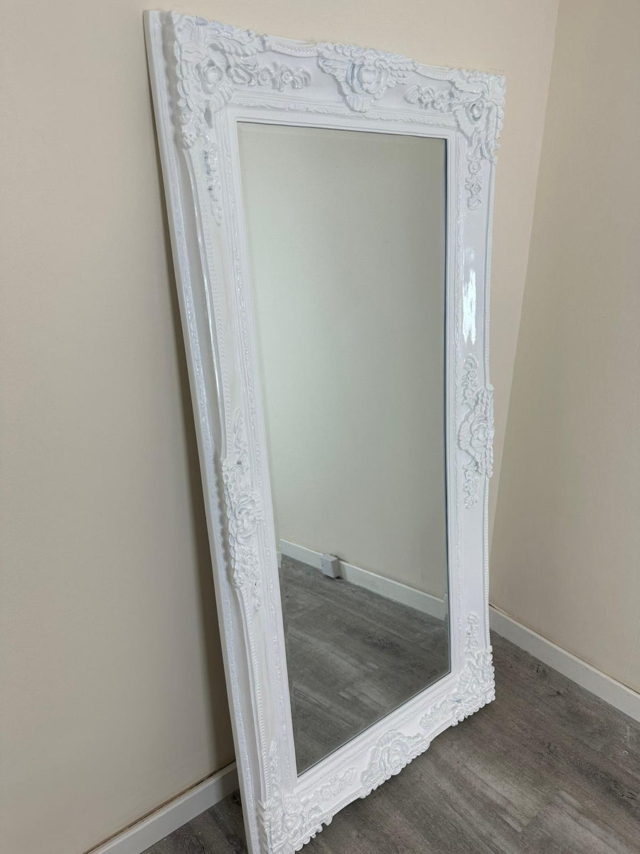 White ornate mirror leaning against a beige wall.